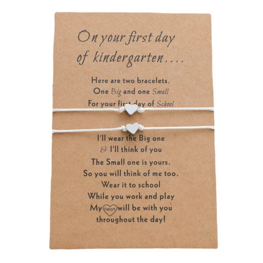 White bracelets with metal heart charms on a brown message card for first day of kindy