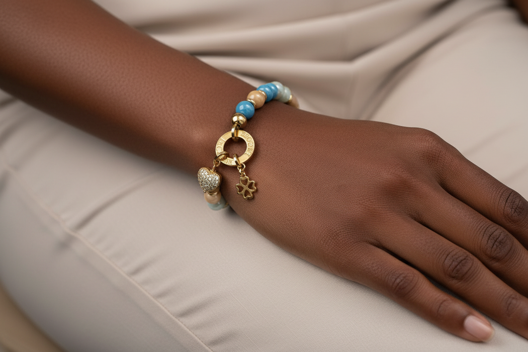 Hand wearing a gold bracelet with blue beads on a beige fabric background