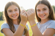 Two young girls holding hands outdoors wearing matching BFF bracelets with a blurred natural background
