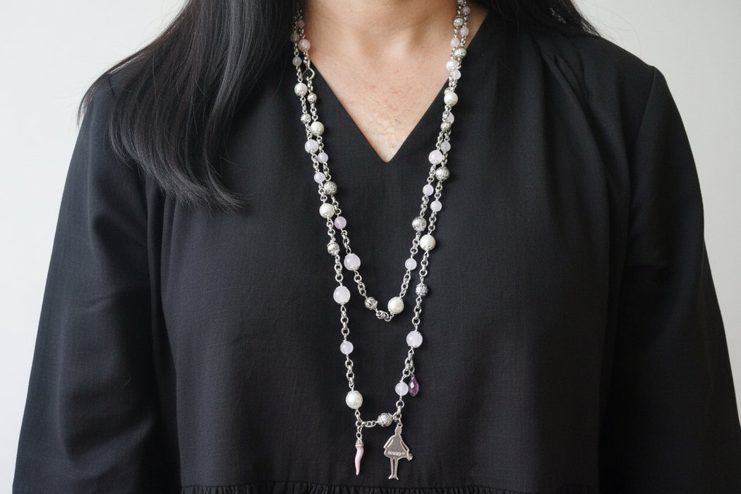 Person wearing a long pearl necklace with black shirt on a plain background
